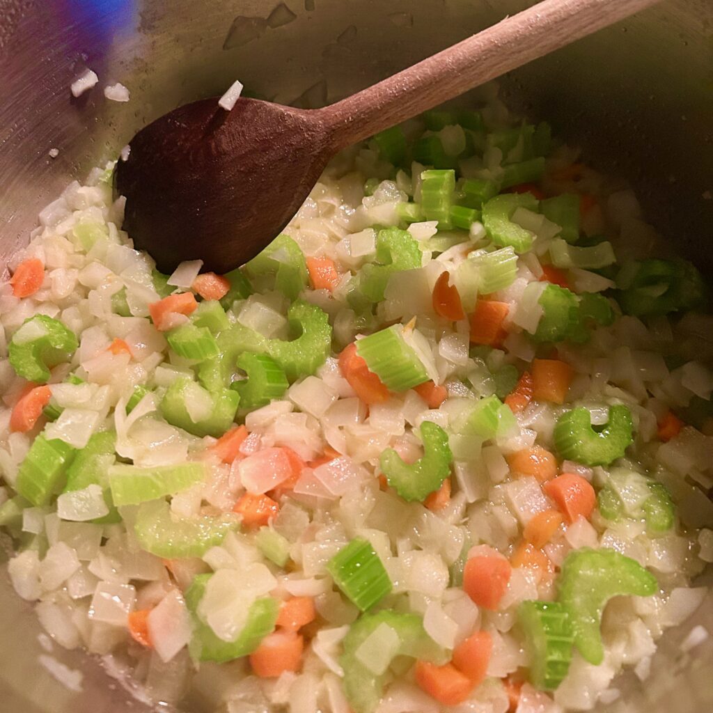 image of chopped onions, carrots, and celery cooking in a stainless steel pot