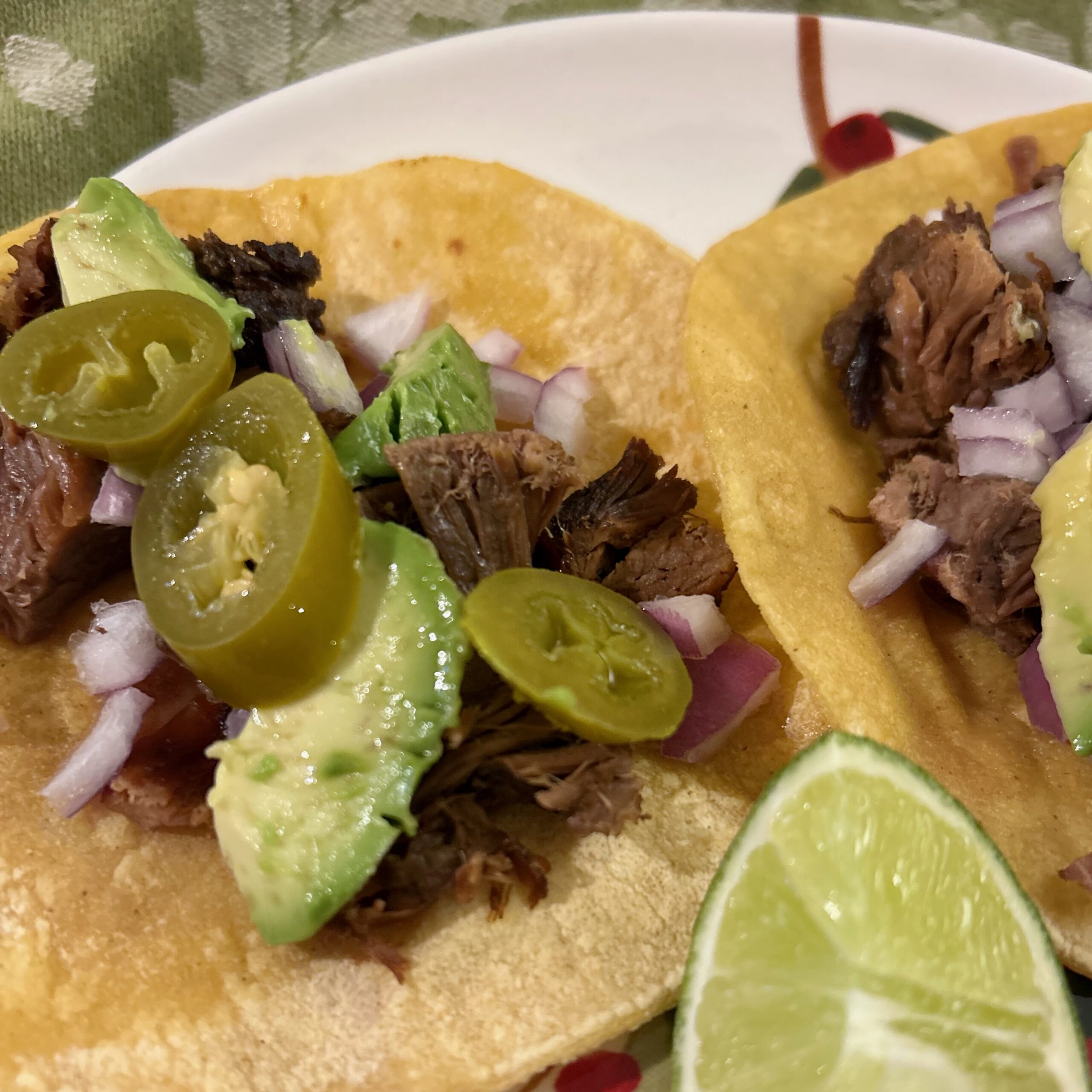 close up of tacos with soft corn tortillas, roast beef, avocado, onion, and jalapeños with a lime wedge on a plate
